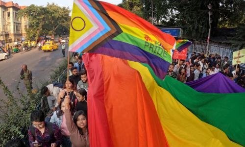 Pride parade through a street with a massive rainbow flag