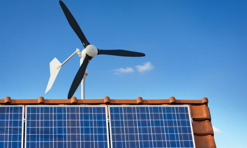 small windmill for small-scale wind energy above a house. Solar panels also atop roof.